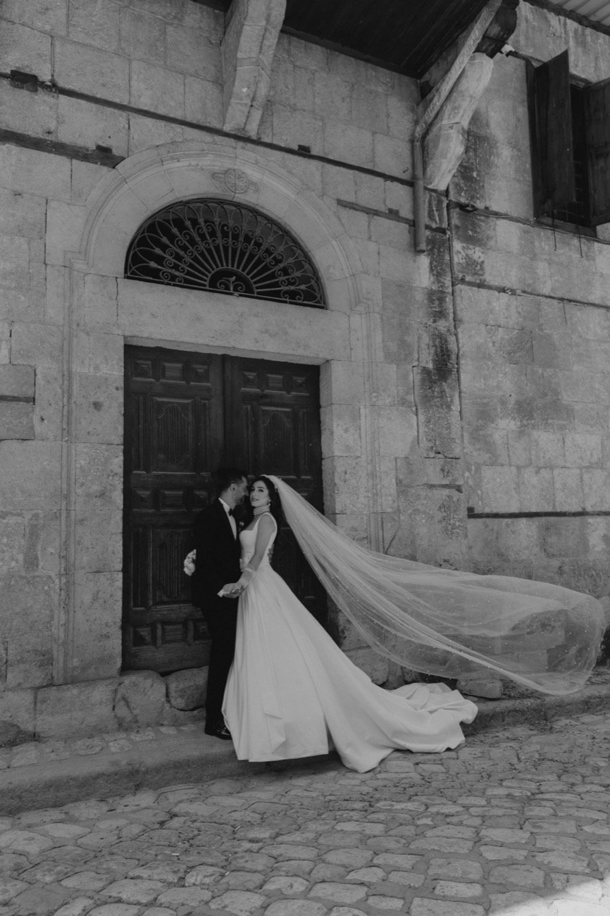 A couple at an old stone doorway, the veil caught by the wind, black and white